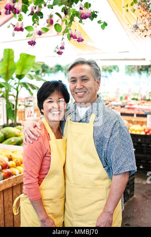 L'homme et la femme propriétaire d'un marché de fruits et légumes, porter des tabliers, côte à côte, souriant à la caméra. Banque D'Images