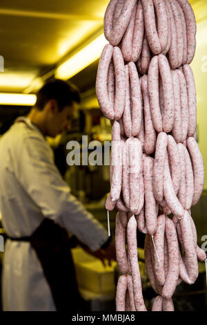 Grand nombre de saucisses fraîchement pendu dans une boucherie, un homme portant un tablier en arrière-plan de travail. Banque D'Images