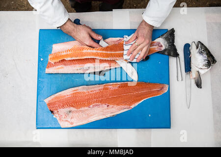 High angle close up of poissonnier debout à une table, de coupe et de filetage bleu saumon frais sur planche à découper. Banque D'Images