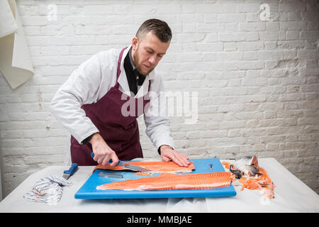 Homme portant un tablier, debout à une table, de coupe et de filetage bleu saumon frais sur planche à découper. Banque D'Images