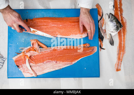 High angle close up of poissonnier debout à une table, de coupe et de filetage bleu saumon frais sur planche à découper. Banque D'Images