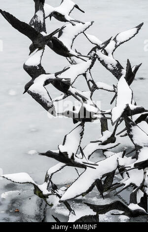 Sculpture d'oiseaux, passant les oiseaux à ailes étendues couvertes de neige en hiver, au-dessus de l'eau. Banque D'Images