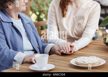 Détient le fournisseur de la main d'une femme âgée, assise à une table avec une tasse de thé Banque D'Images