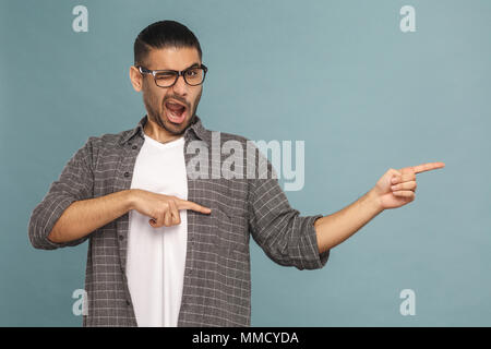 Portrait de bel homme drôle barbu à lunettes noires style décontracté à la caméra et au pointage et montre copyspace sur arrière-plan. studio shot sur Banque D'Images