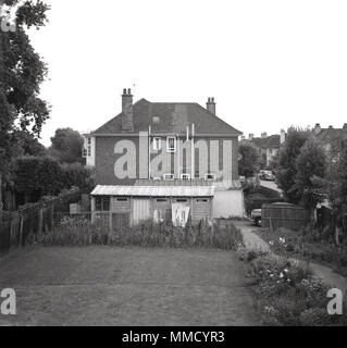 Début des années 60, vue extérieure d'une grande maison et des garages à côté verdoyant de Hanwell, Ealing, London, England, UK. Banque D'Images