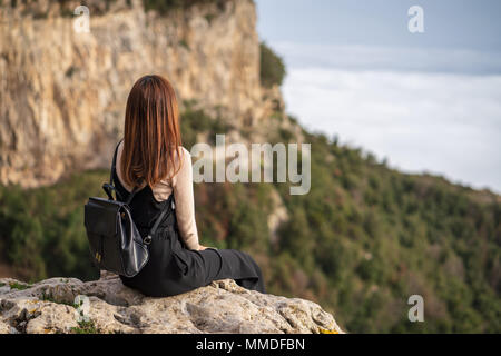 Jeune femme avec sac à dos noir assis sur le bord de la falaise et admirer la vue de paysage de montagne lors de votre randonnée sur la montagne de Positano, Italie. Banque D'Images