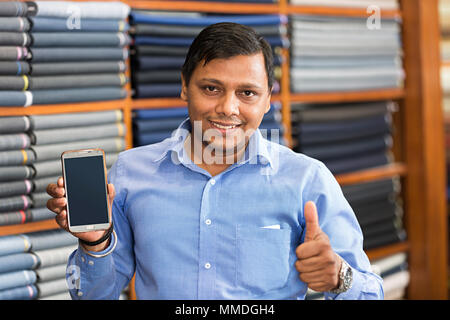 Un vendeur Showing Thumbs-up avec Smart Phone In clothes store Banque D'Images