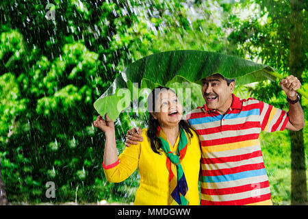 Vieux couple heureux sous les feuilles de bananes, de protéger de la pluie en Fun-Cheerful ont-jardin Banque D'Images