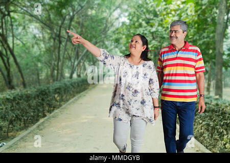 Happy Senior Couple Walking et Doigt montrant dans jardin Banque D'Images