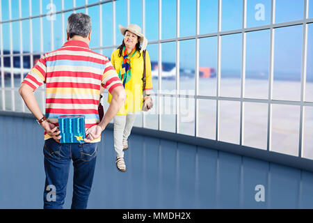 Heureux couple, mari Holding gift derrière pour surprendre Femme In-Airport Banque D'Images