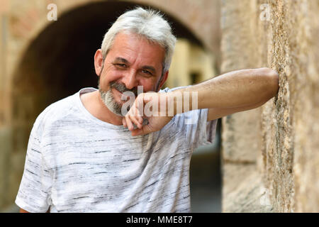 Man smiling at camera en contexte urbain. Le plus âgé avec des cheveux blancs et sa barbe portant des vêtements décontractés. Banque D'Images