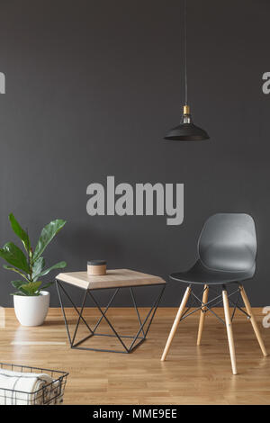 Plante, simple chaise et table basse en bois fixés sur noir, mur vide dans le salon intérieur Banque D'Images