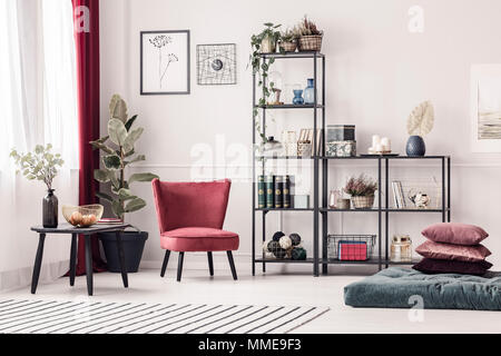 Fauteuil en velours rouge, à côté d'un rack en métal noir, avec décorations debout contre un mur blanc avec bandeau en salon lumineux intérieur Banque D'Images