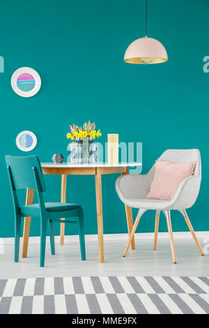 Chaise, fauteuil avec coussins, table à manger, le bar et les plaques de tapis sur un mur vert dans un décor intérieur salle à manger Banque D'Images