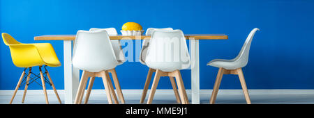 Bleu royal minimaliste de l'intérieur salle à manger avec une grande table en bois et plastique moderne chaises jaune et blanc Banque D'Images