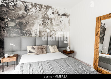 Le gris et le blanc de l'intérieur chambre à coucher moderne avec table de chevet en bois rustique, grand miroir et abstract grunge décor mural Banque D'Images