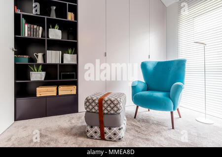 Intérieur moderne avec coin lecture avec bibliothèque noir, bleu fauteuil, pouf et grande fenêtre avec stores Banque D'Images