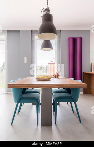 Salle à manger moderne de l'intérieur avec table en bois, chaises, lampes industrielles turquoise et violet du radiateur de chauffage Banque D'Images