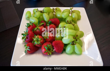 Plaque blanche avec des raisins verts et les fraises. Banque D'Images