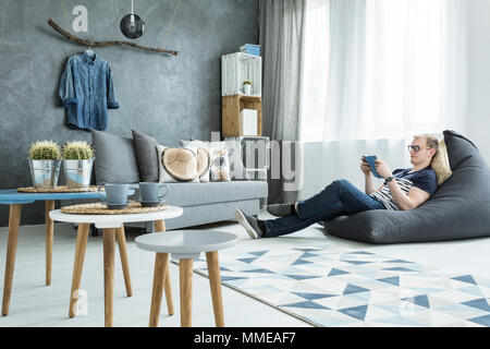 Intérieur de style moderne en gris avec un canapé élégant, futniture, homme assis sur un sac de haricots Banque D'Images