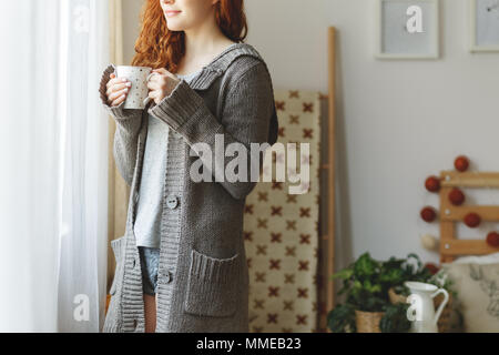 Smiling woman in sweater en regardant par la fenêtre Banque D'Images