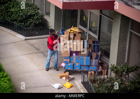 Un livreur de Lasership avec son chariot chargé d'achats de l'aime de Amazon, tablier bleu, et d'autres sortes ses livraisons à un immeuble le quartier de Chelsea, New York le lundi 30 avril, 2018 . (Â©Â Richard B. Levine) Banque D'Images