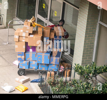 Un livreur de Lasership avec son chariot chargé d'achats de l'aime de Amazon, tablier bleu, et d'autres sortes ses livraisons à un immeuble le quartier de Chelsea, New York le lundi 30 avril, 2018 . (Â©Â Richard B. Levine) Banque D'Images