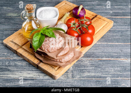 Pile d'escalopes de burgers de poulet sur une planche en bois avec des tomates cerises et d'épices. Banque D'Images