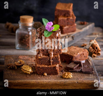 Une pile de tarte Brownie cuit sur une planche de bois brun, un dessert est coulé d'une épaisse couche de chocolat et décoré de feuilles de menthe et une fleur Banque D'Images