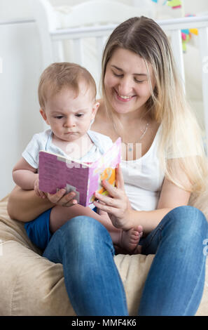 Portrait of smiling jeune mère assise sur le fer avec son bébé garçon et lui livre de lecture Banque D'Images