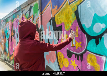 Vue arrière d'une personne portant un sweat de pulvériser un graffiti sur un mur, la criminalité de rue concept. Banque D'Images