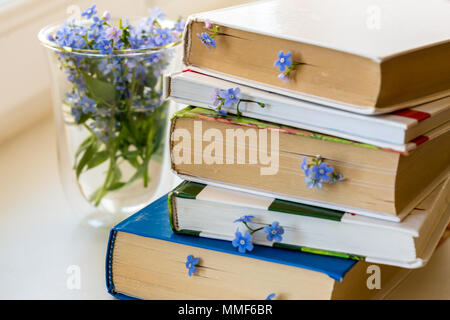 Une pile de livres avec de petites fleurs bleu entre les pages sur tableau blanc Banque D'Images
