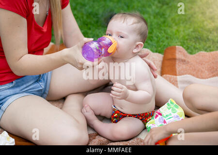 Cute baby boy sitting on blanket sur pique-nique en famille et boire du jus de la bouteille Banque D'Images