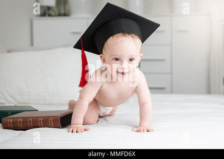 Image drôle de bébé adorable garçon aux couches portant graduation cap ramper sur le lit Banque D'Images