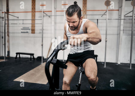 Mettre en place en jeune homme sportswear équitation centrée sur un vélo stationnaire pendant une séance d'entraînement à la salle de sport Banque D'Images