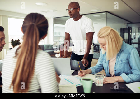 African businessman leaning on parle d'une chaise avec des collègues au cours d'une réunion autour d'une table dans un bureau moderne Banque D'Images