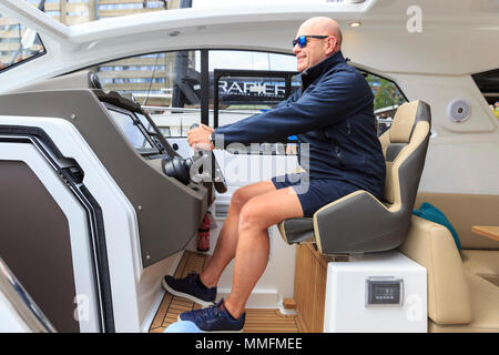 St Katherine Docks, Londres, 11 mai 2018. Richard Cottrell, Responsable des ventes pour l'Azimut, est assis confortablement sur la roue du yacht. Maintenant à sa quatrième année et tenue à l'emblématique marina à côté du coeur de la ville de Londres et du Tower Bridge, Londres est une une un Boat Show et festival, où les yachts, bateaux, voitures et une foule d'autres entreprises peuvent être envisagées à la fois sur l'eau et sur terre. Il s'étend du 10 au 12 mai. Credit : Imageplotter News et Sports/Alamy Live News Banque D'Images