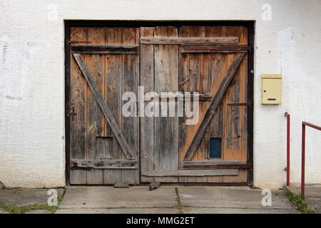 Portes de garage en bois délabrée vieille avec charnières métalliques rouillées et petites lettres monté sur le côté droit du mur blanc Banque D'Images