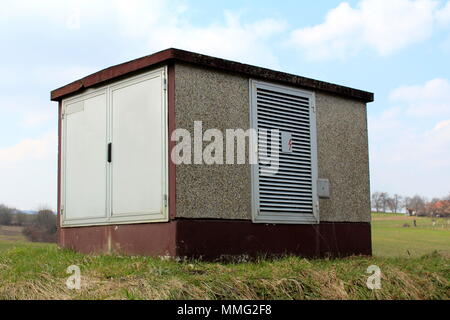 Béton extérieur haute tension électrique fort avec deux portes de métal et d'un côté l'ouverture de ventilation haute entourée d'herbe non coupée et ciel nuageux dans Banque D'Images