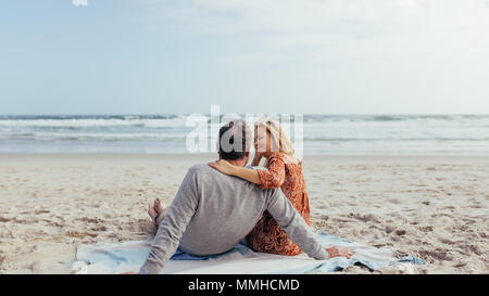 Vue arrière shot of man and woman sitting on beach towel le long du bord de mer. Couple romantique de détente sur la plage. Banque D'Images