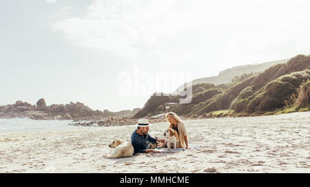 Senior couple relaxing on beach sable avec leurs chiens de compagnie. L'homme et la femme mature avec les chiens sur la rive à matin. Banque D'Images