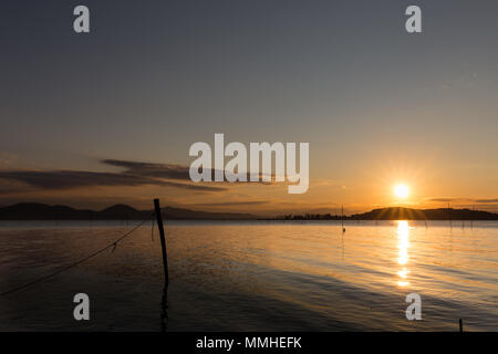 Magnifique coucher de soleil sur le lac Trasimeno (Ombrie), avec du soleil qui descend derrière une île et quelques filets de pêche dans l'avant-plan Banque D'Images