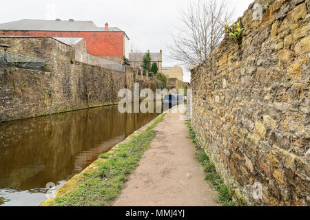 Sur une journée terne le canal de Leeds et Liverpool reflète les bâtiments voisins dans sa surface. Au loin une barge est amarré sur un coude. Banque D'Images