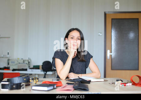 Belle femme assise à l'atelier de cuir et en faisant de l'ordinateur portable à la main, smartphone sur table. Banque D'Images
