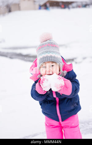 Petite fille emmitouflés en rose et bleu joyeusement snow Banque D'Images