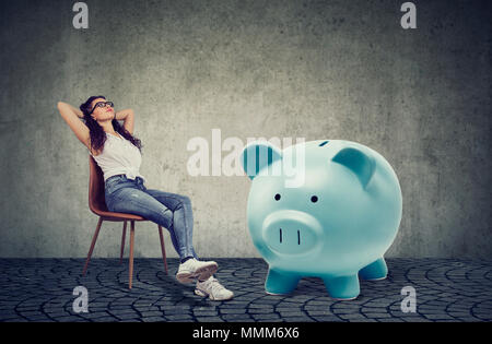 Jeune femme avec grande tirelire relaxing sitting on chair Banque D'Images