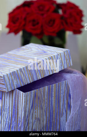 Boîte avec un cadeau sur fond d'un bouquet de roses rouges Banque D'Images