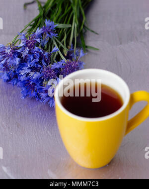 Tasse de thé jaune et un bouquet de barbeaux sur une table violet Banque D'Images