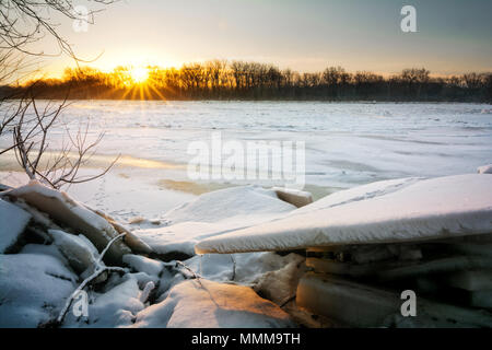 Un bel hiver enneigé lever du soleil le long de la rivière Maumee gelés dans le nord-ouest de l'Ohio. Énormes morceaux de glace brisée a été poussé jusqu'au bord de la ri Banque D'Images