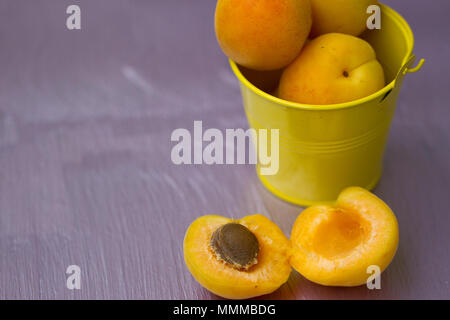 Les abricots dans un petit seau jaune sur table violet Banque D'Images